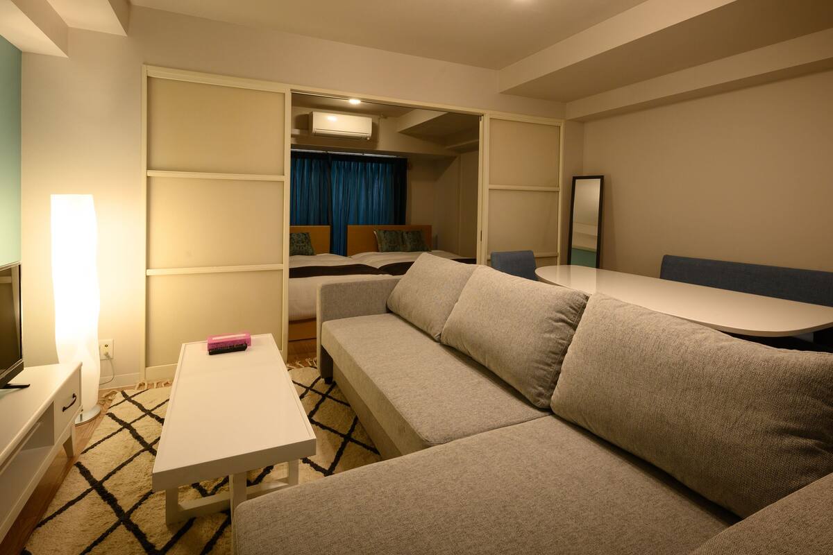 A hotel room with a sofa, a TV, a small table, and a mirror.