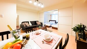 Une pièce bien éclairée, avec une table à manger dressée pour deux personnes, un canapé, un lit et un téléviseur.