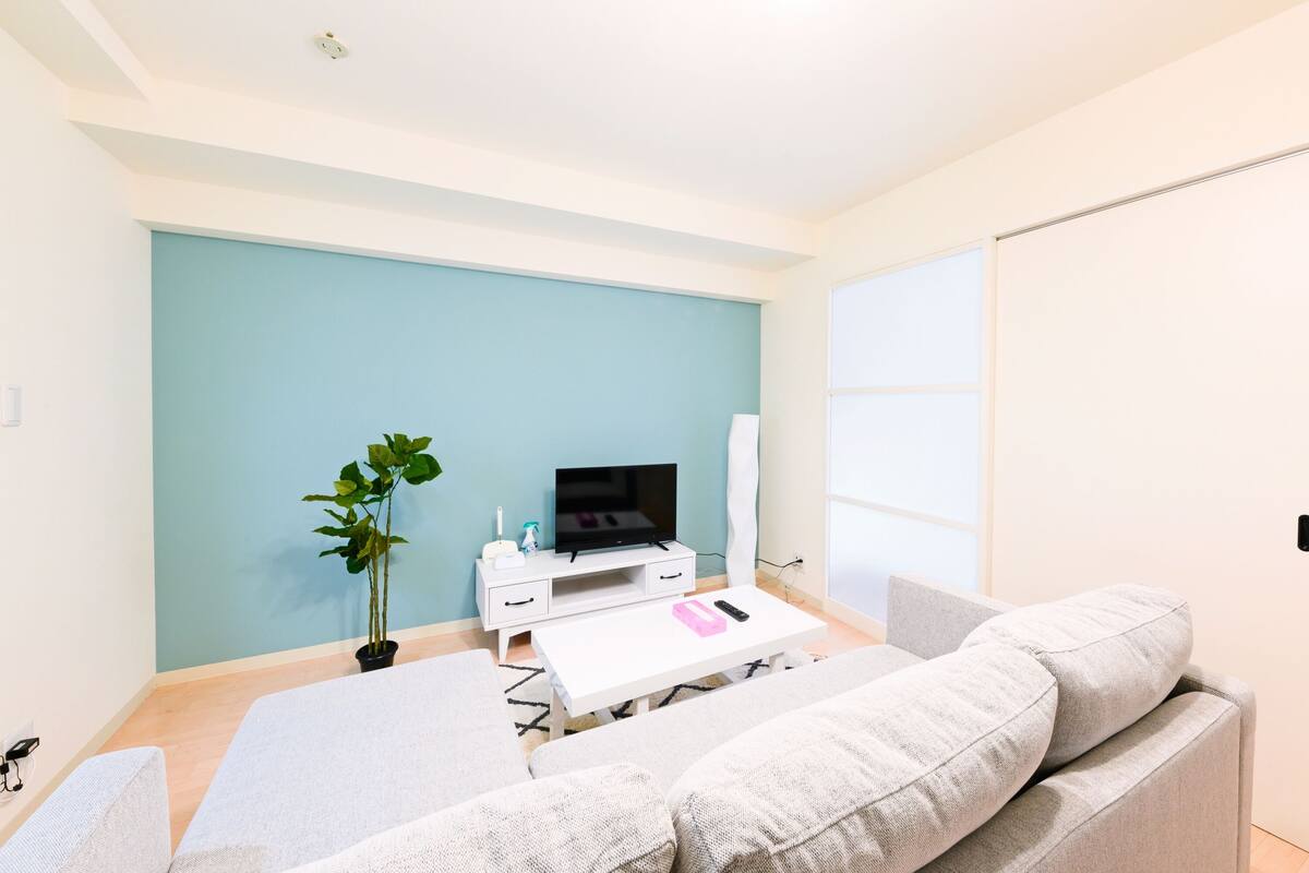 A modern living room with a white sofa, a white coffee table, a flat-screen TV, and a potted plant.