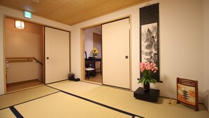 A traditional Japanese room with tatami flooring, sliding doors, a small table with a vase of flowers, and a framed artwork on the wall.