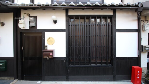 A traditional Japanese building with a black and white facade, a sliding door, and a red mailbox.