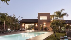 Une maison moderne dotée d’une piscine, de chaises longues et d’un jardin bien entretenu.