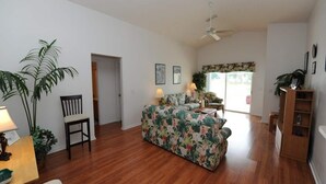 A spacious living room with a wooden floor, a floral sofa, a dining table with chairs, and a ceiling fan. - Lake Therapy, Experience the ultimate vacation getaway in vibrant Caggans Crossing. (Clermont)