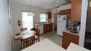 A compact kitchen with wooden cabinets, a refrigerator, a stove, and a dining table with chairs. - Lake Therapy, Experience the ultimate vacation getaway in vibrant Caggans Crossing. (Clermont)