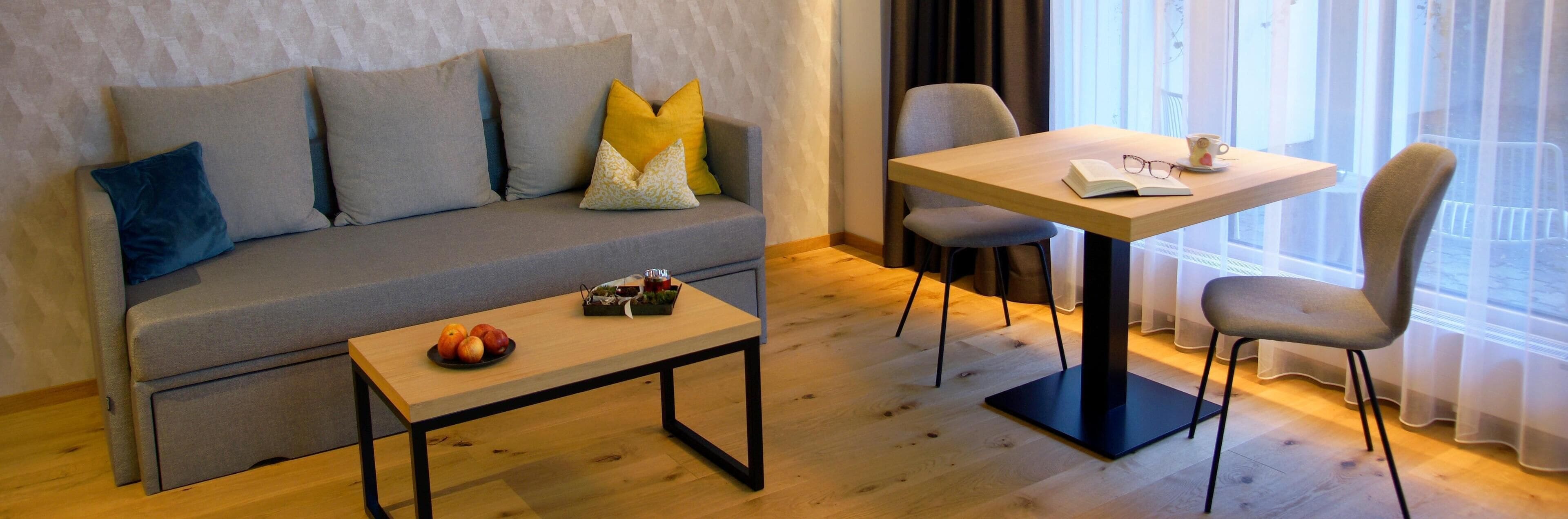 A modern living room with a grey sofa, a wooden coffee table with fruits, and a dining area with a table and chairs.
