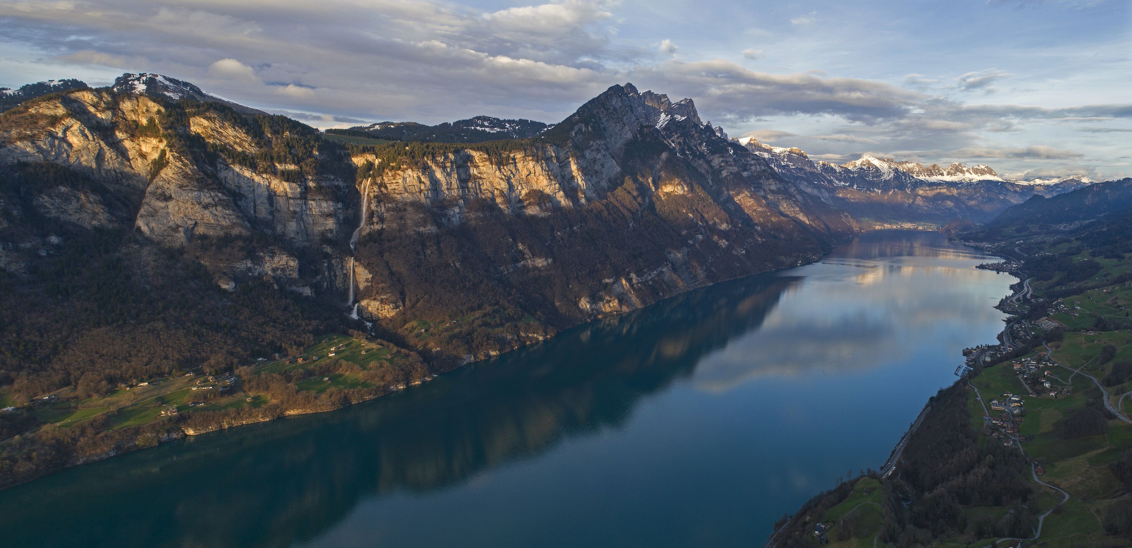 Un paisaje montañoso con un lago, un camino sinuoso y un pequeño asentamiento.