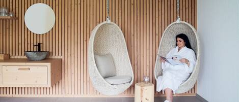 Una habitación con dos sillas colgantes, un muro de madera, un espejo redondo, un armario de madera y una pequeña mesa redonda.