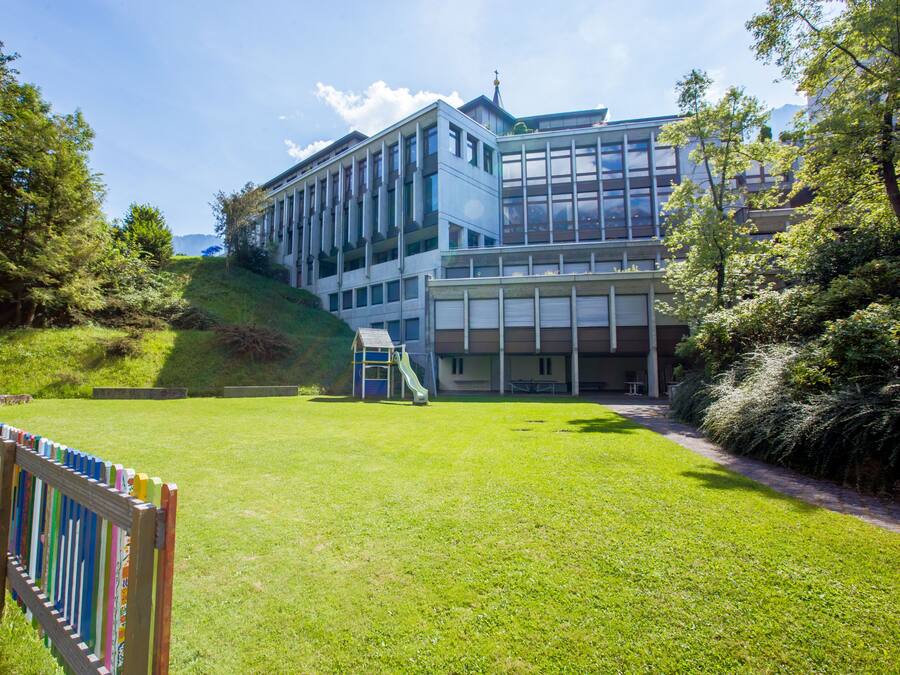 A modern building with a large glass facade, a playground, and a grassy area.