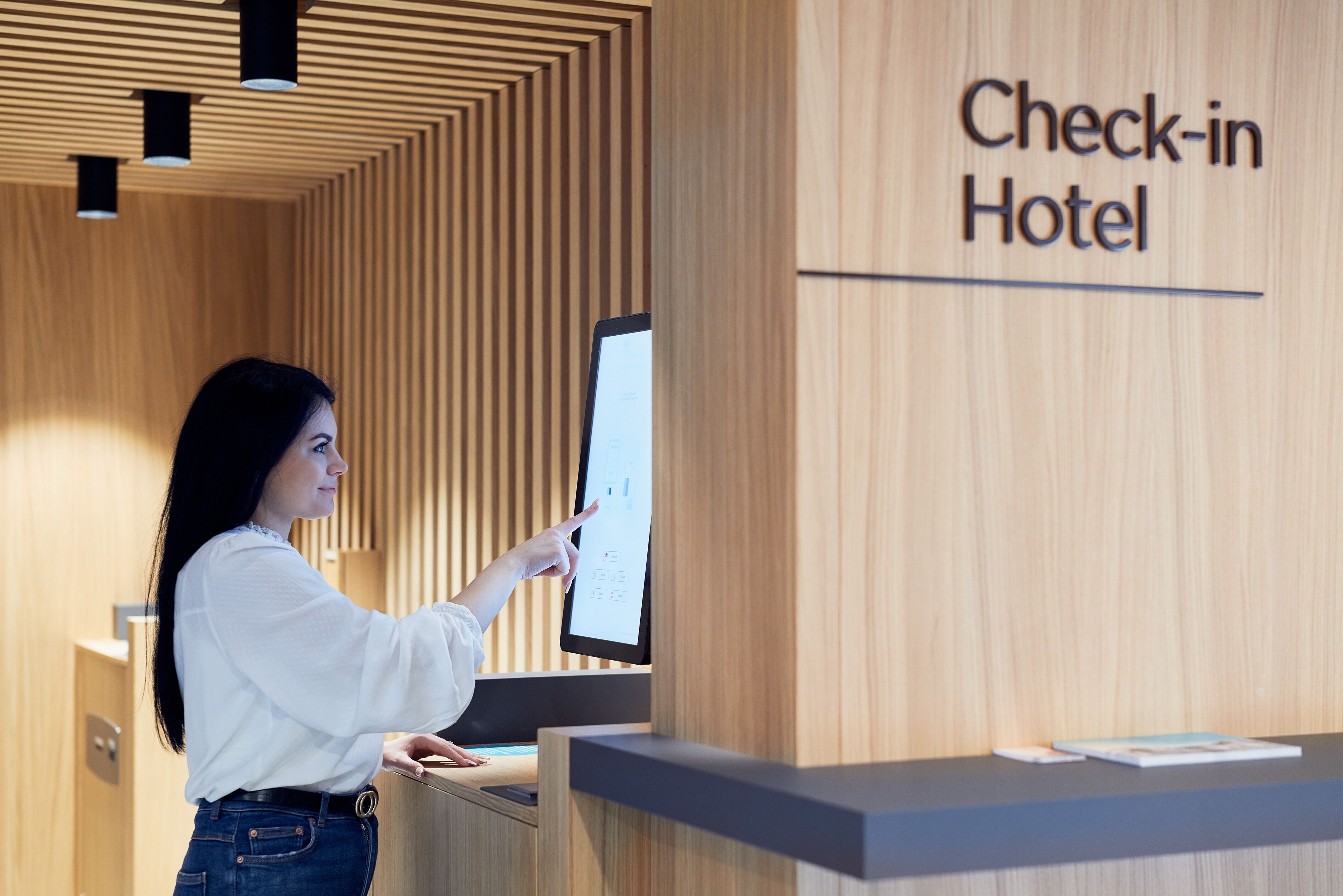 A woman interacting with a digital kiosk at a hotel reception area.