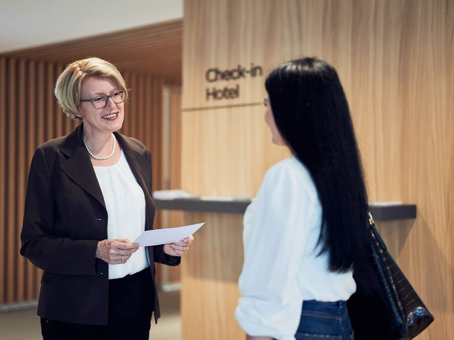 Two people in a hotel lobby with a 'Check-in Hotel' sign.
