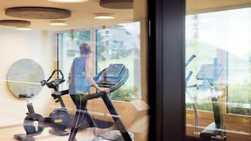 Ein Fitnessstudio mit Trainingsgeräten, großen Fenstern und einer Holzbalkendecke.