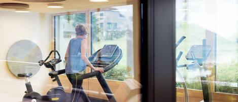 A gym with exercise equipment, large windows, and a wooden ceiling.