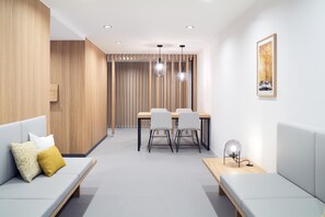 A modern hotel room with a wooden accent wall, a dining area with a table and chairs, a sofa with cushions, and a bedside table with a lamp. - Hotel Neu-Schönstatt (Quarten)