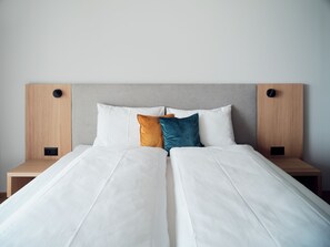 A neatly made bed with white linens, two pillows, and a headboard with two speakers. - Hotel Neu-Schönstatt (Quarten)