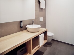 A modern bathroom with a wooden vanity, a white sink, and a toilet. - Hotel Neu-Schönstatt (Quarten)