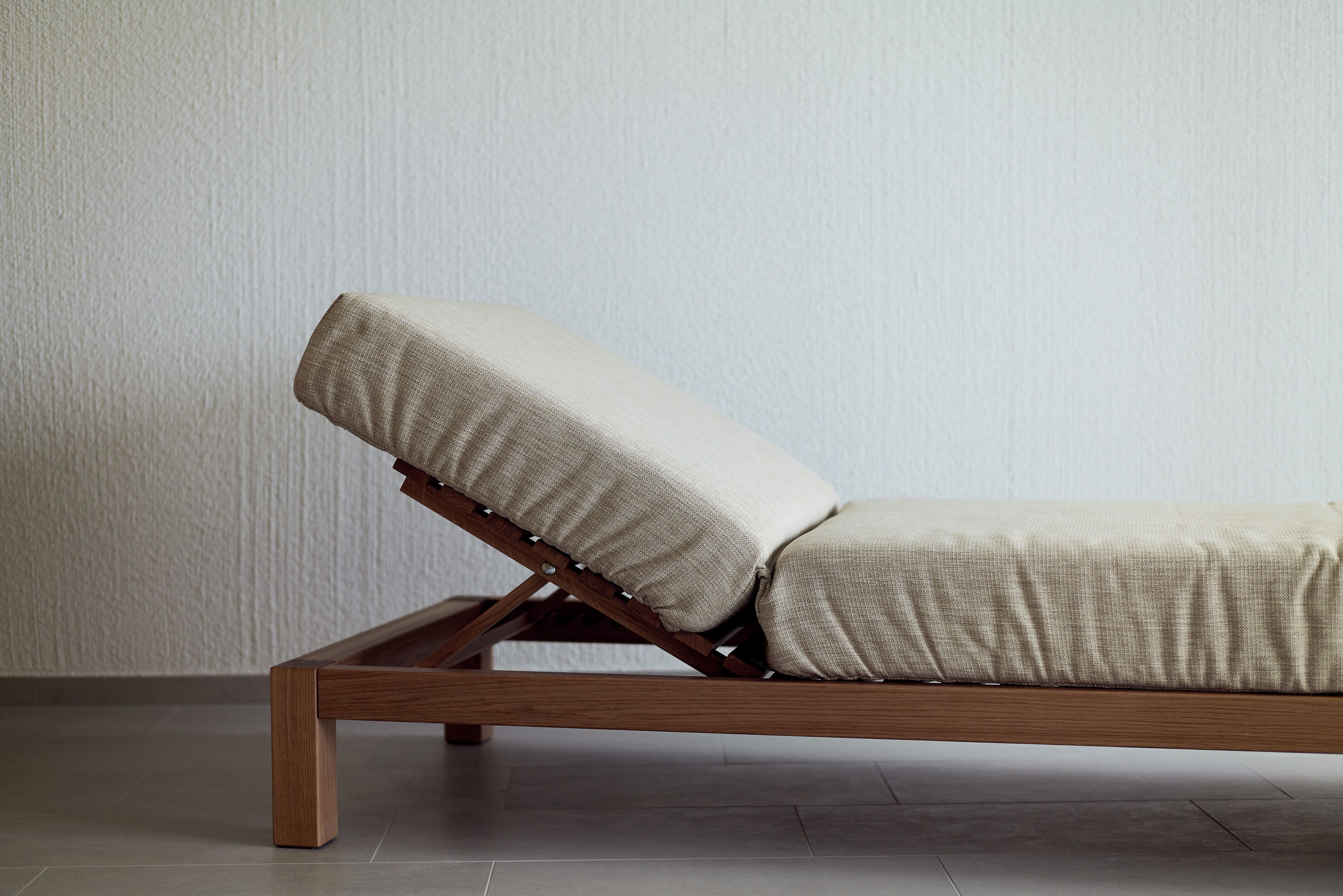 Ein moderner Lounge-Sessel mit Holzgestell und beigen Kissen, vor einer schlichten Wand mit Fliesenboden platziert.