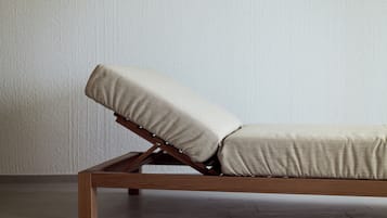 Ein moderner Lounge-Sessel mit Holzgestell und beigen Kissen, vor einer schlichten Wand mit Fliesenboden platziert.