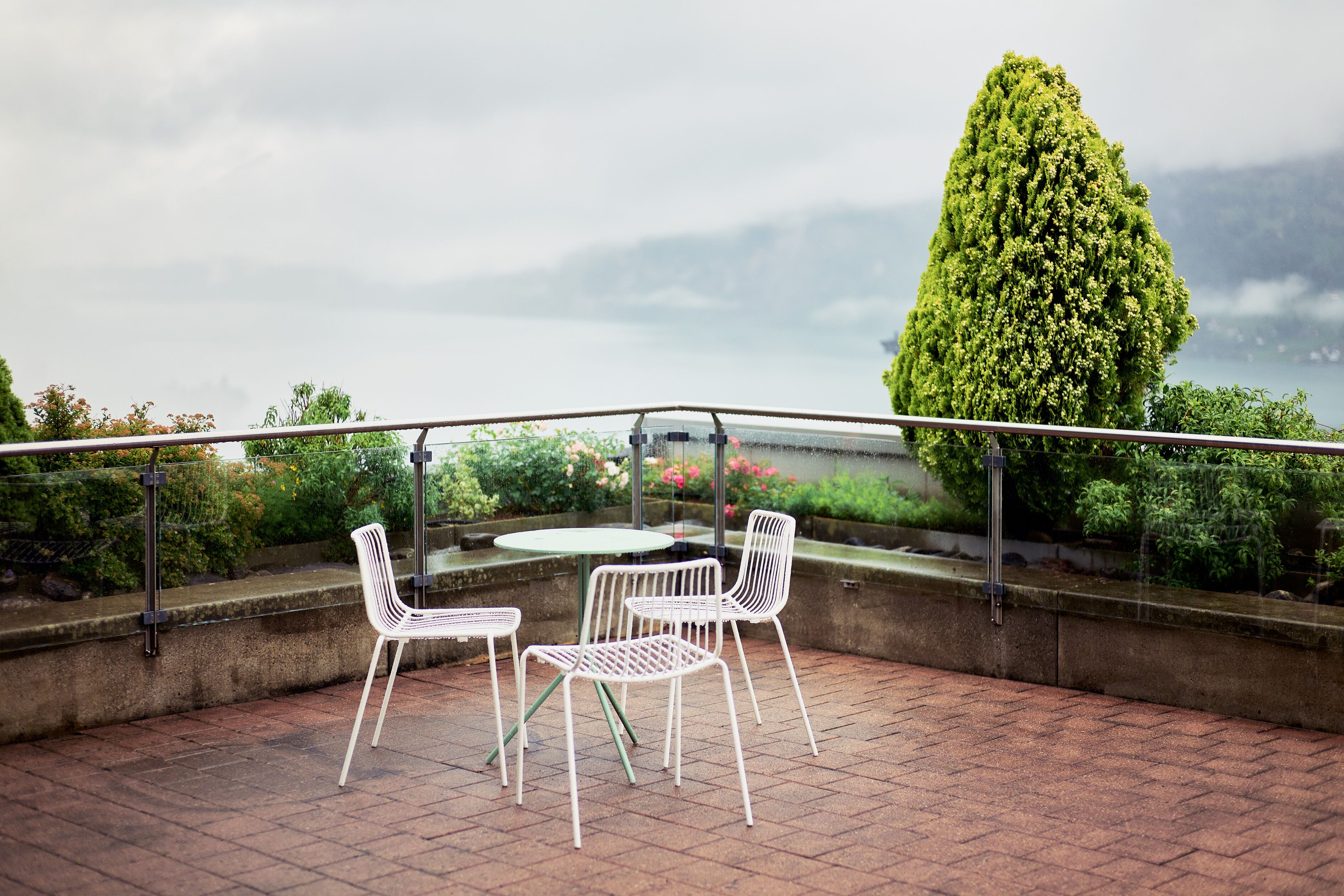 A terrace with a table and chairs, overlooking a garden and a body of water.