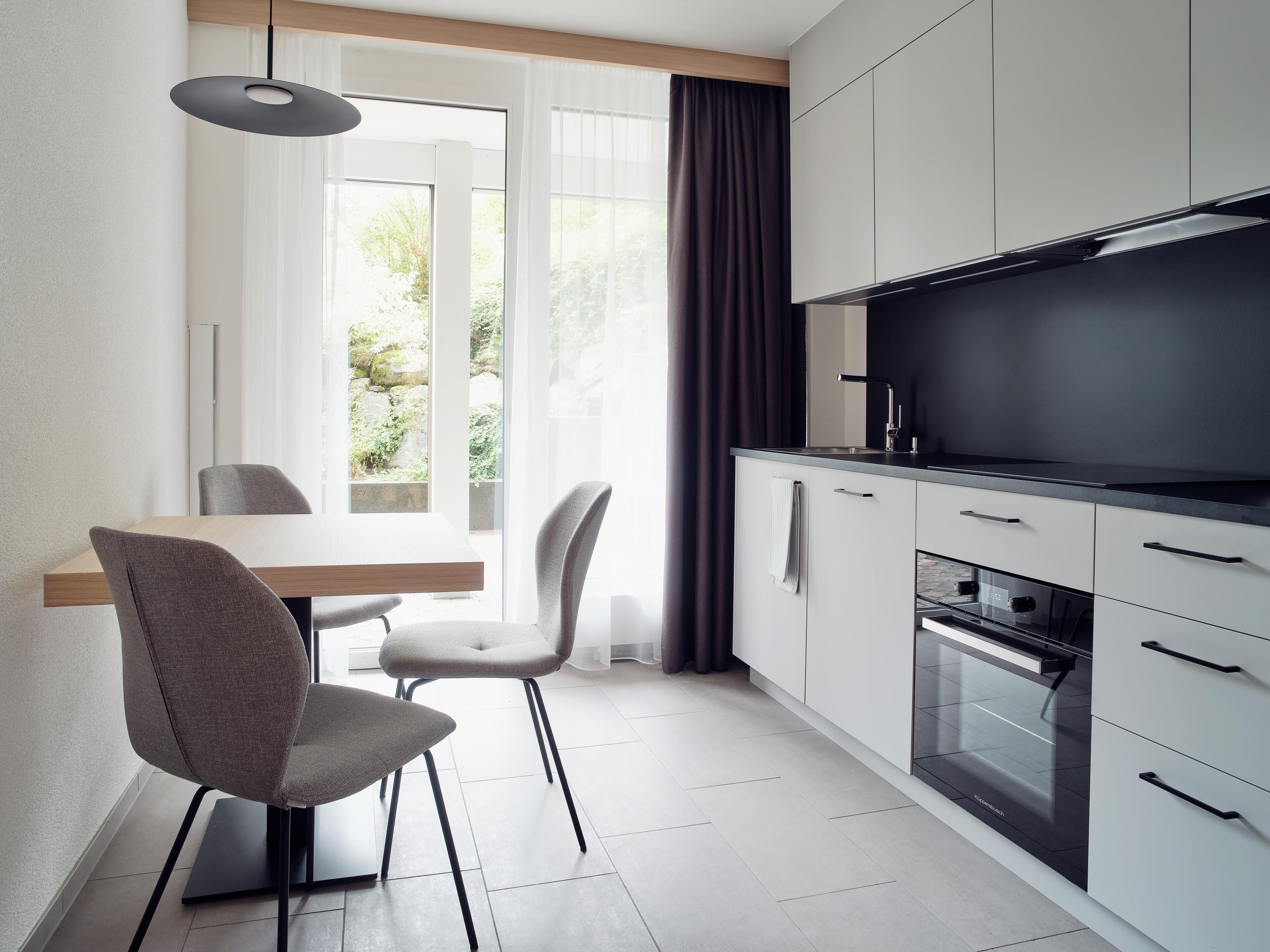 A modern kitchen with a dining area, featuring a large window, a built-in oven, and a flat-screen TV.
