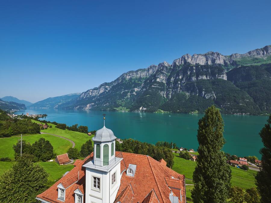 A church with a bell tower overlooking a lake and mountains.