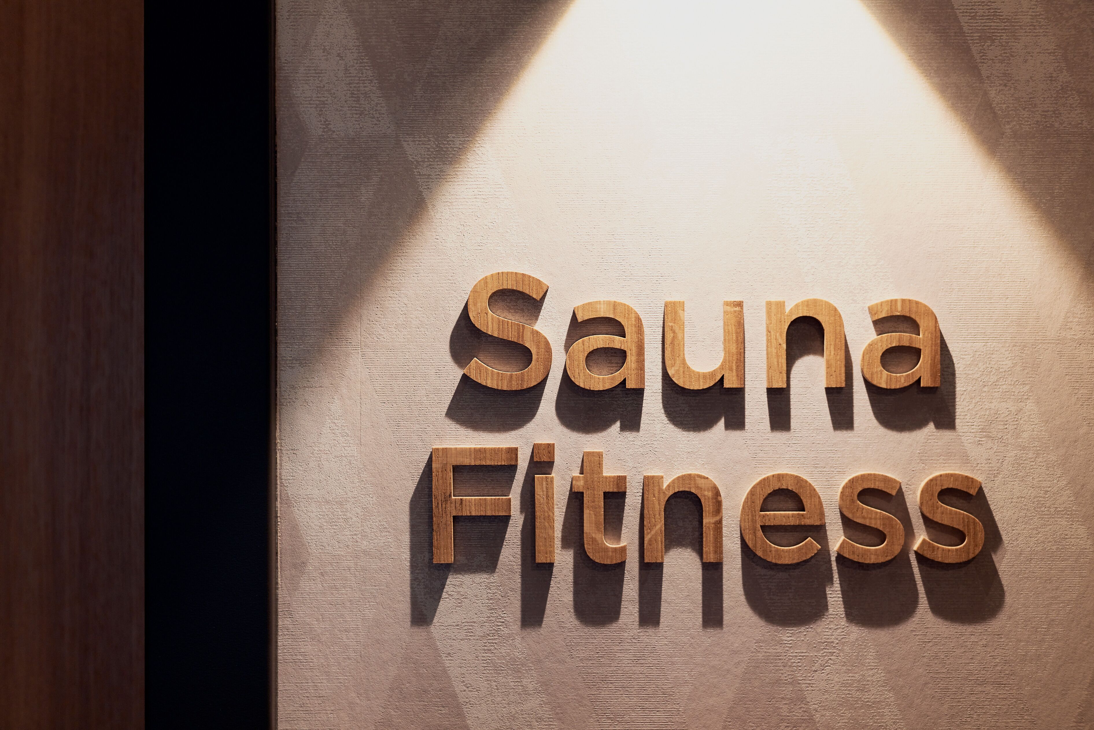 Wooden letters spelling "Sauna Fitness" on a wall.