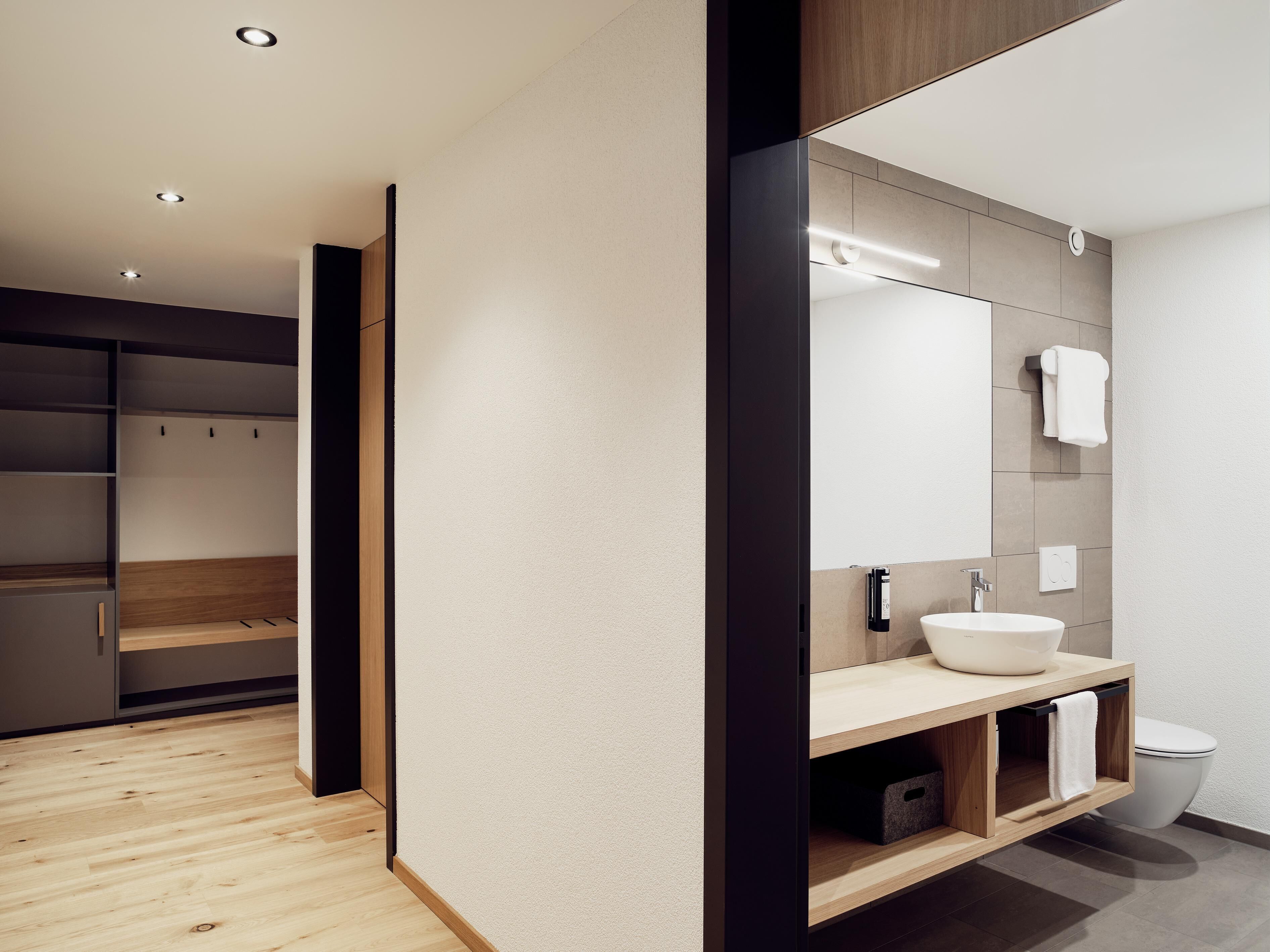 Ein modernes Badezimmer mit einem Holzbadezimmerunterschrank, einem großen Spiegel und einem weißen Waschbecken.