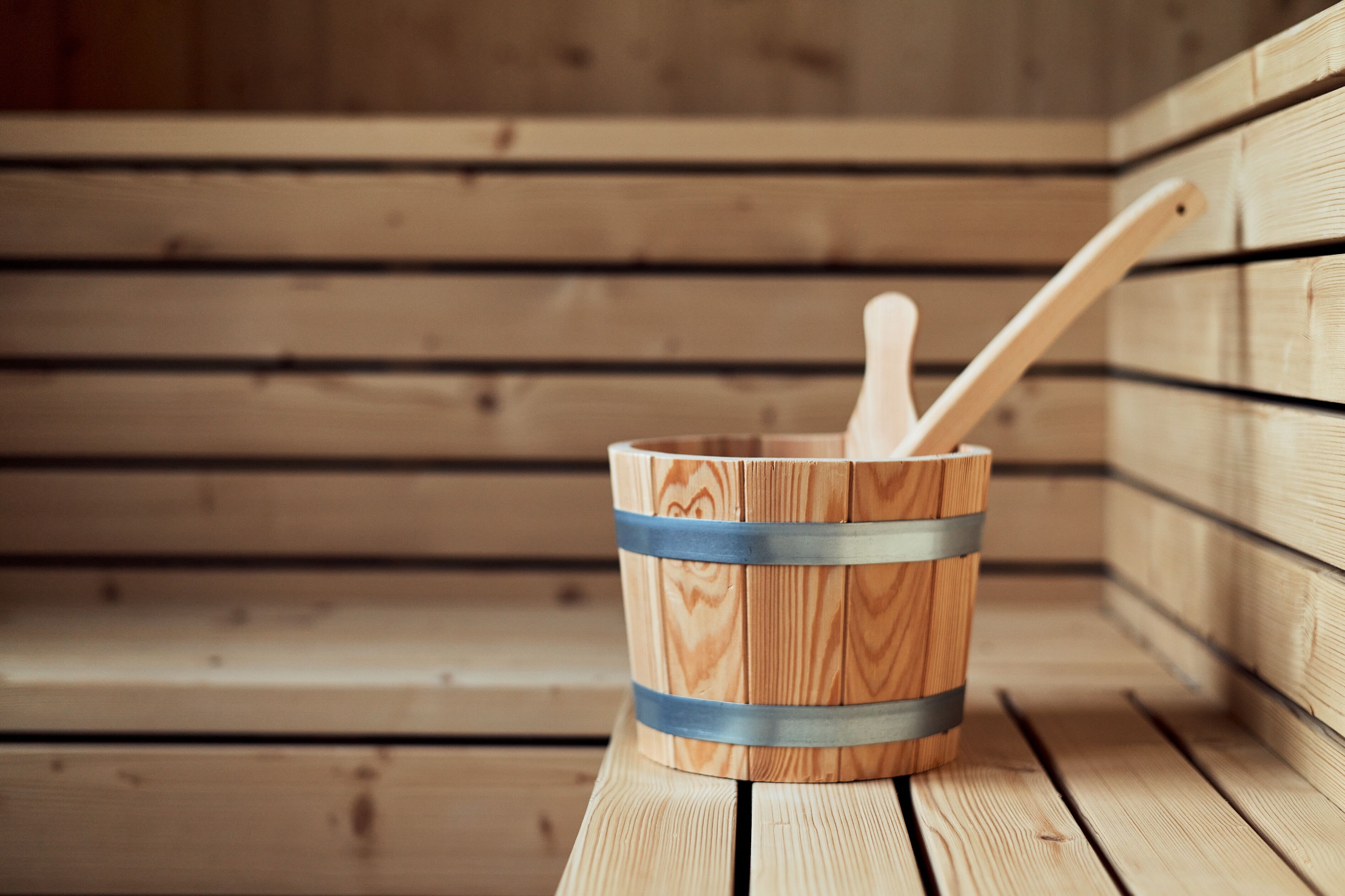 A wooden bucket with a wooden spoon inside, placed on a wooden bench in a sauna room.
