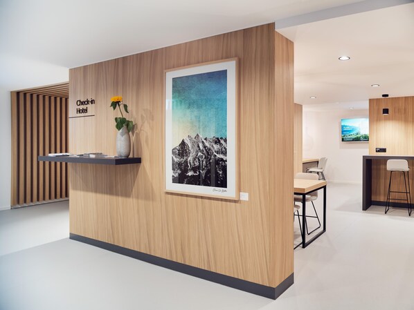 A hotel reception desk with a 'Check-in Hotel' sign, a framed mountain landscape poster, and a vase with flowers. - Hotel Neu-Schönstatt (Quarten)