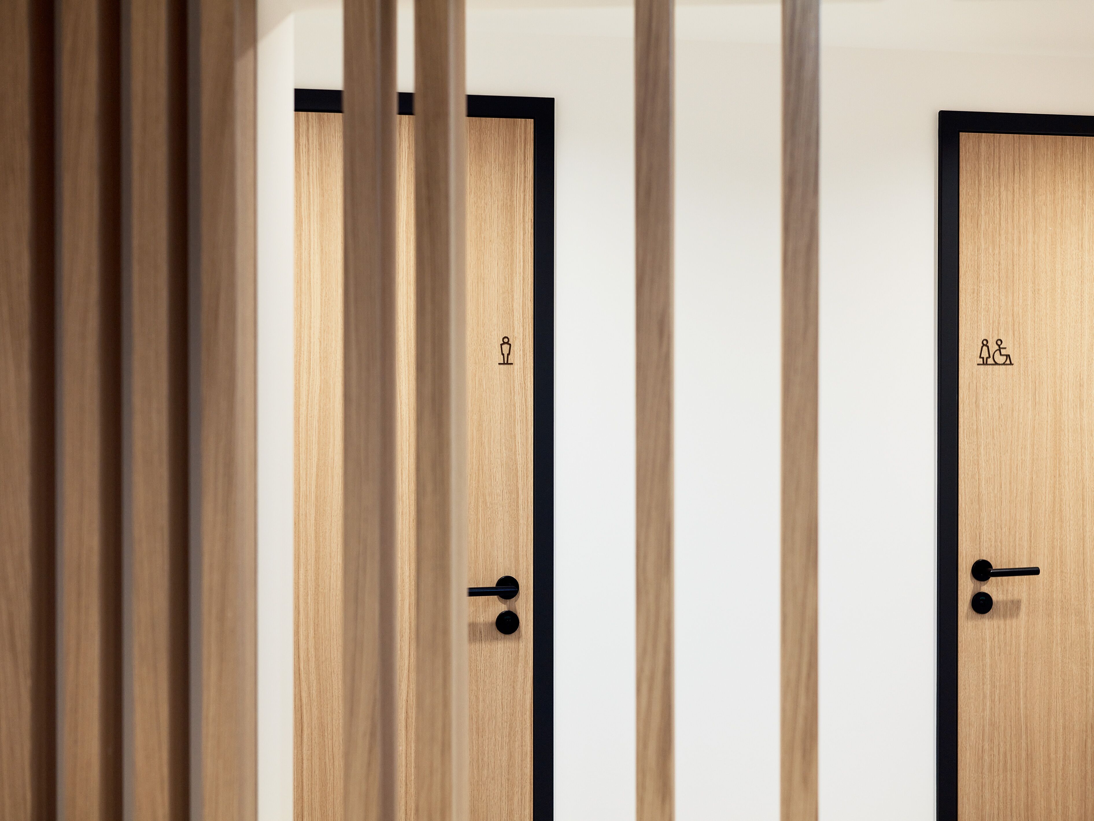 Two wooden doors with black frames, each marked with a single icon indicating a restroom.