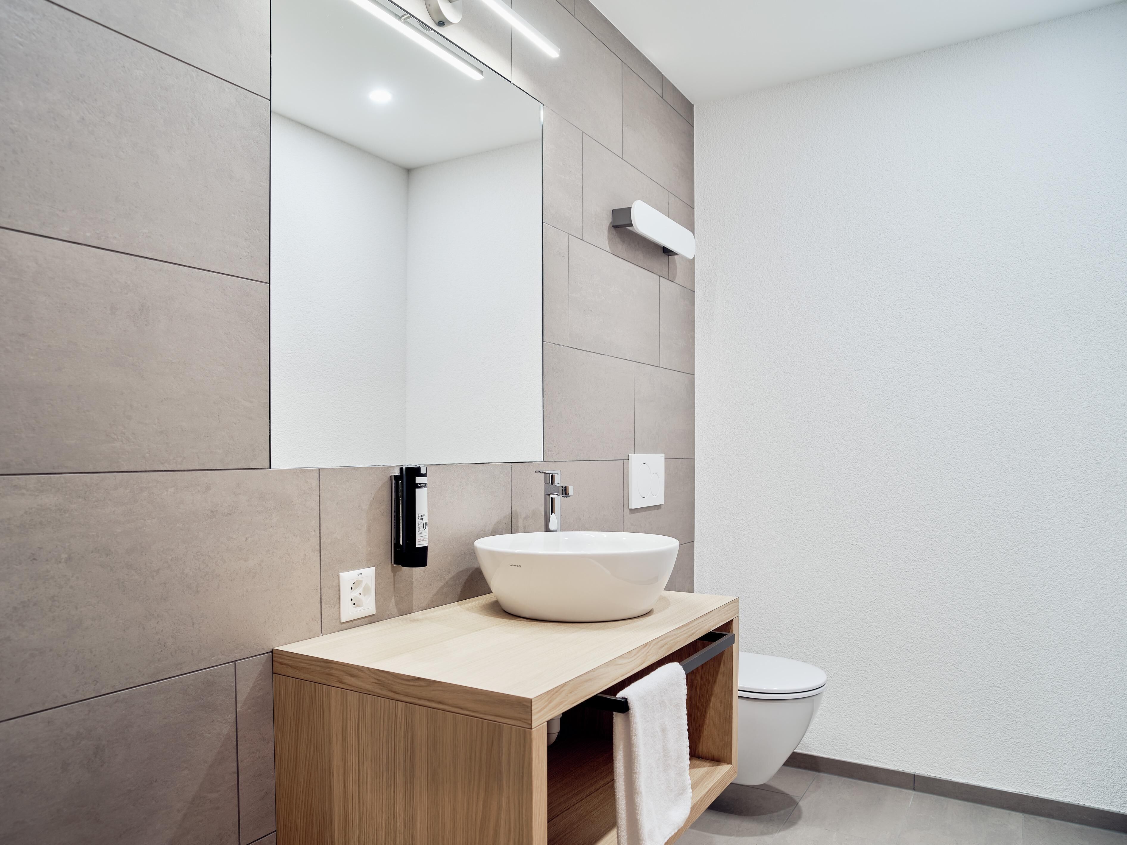 Ein modernes Badezimmer mit einem großen Spiegel, einem Aufsatzwaschbecken und einer Toilette.