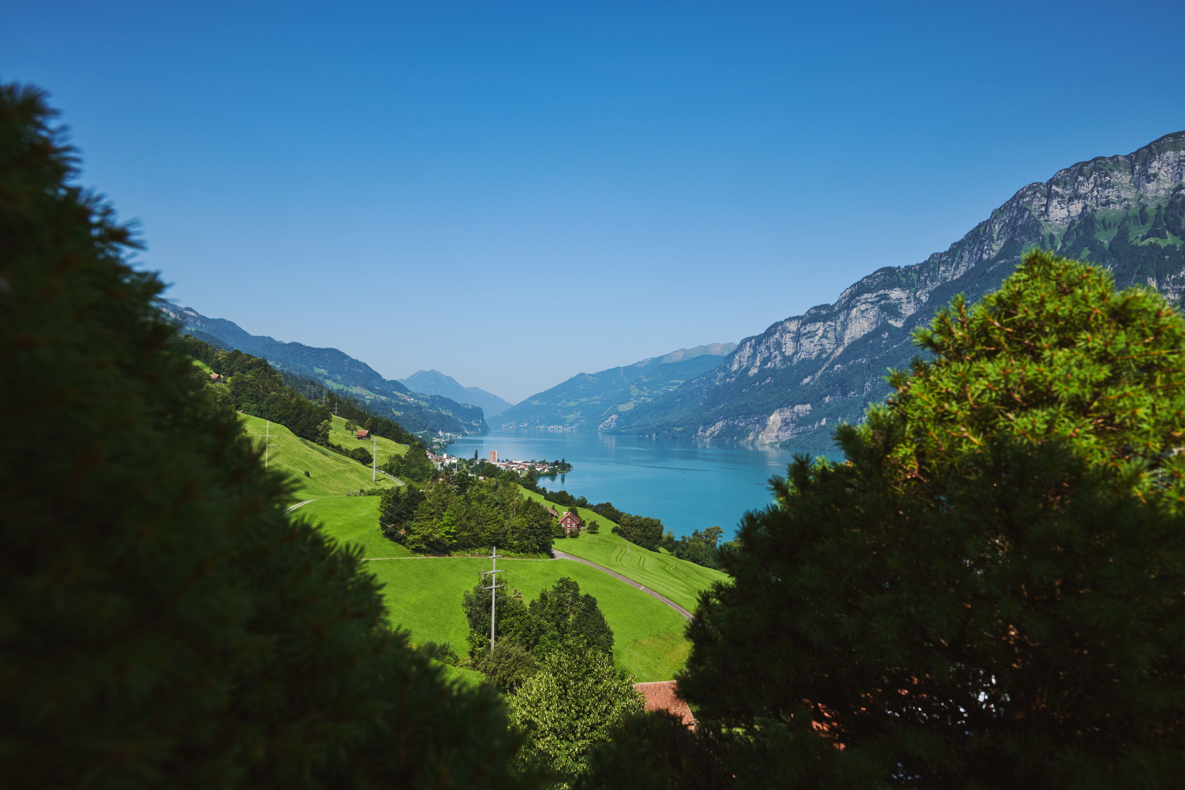 Un paysage montagneux avec un lac, entouré de verdure et de quelques bâtiments.