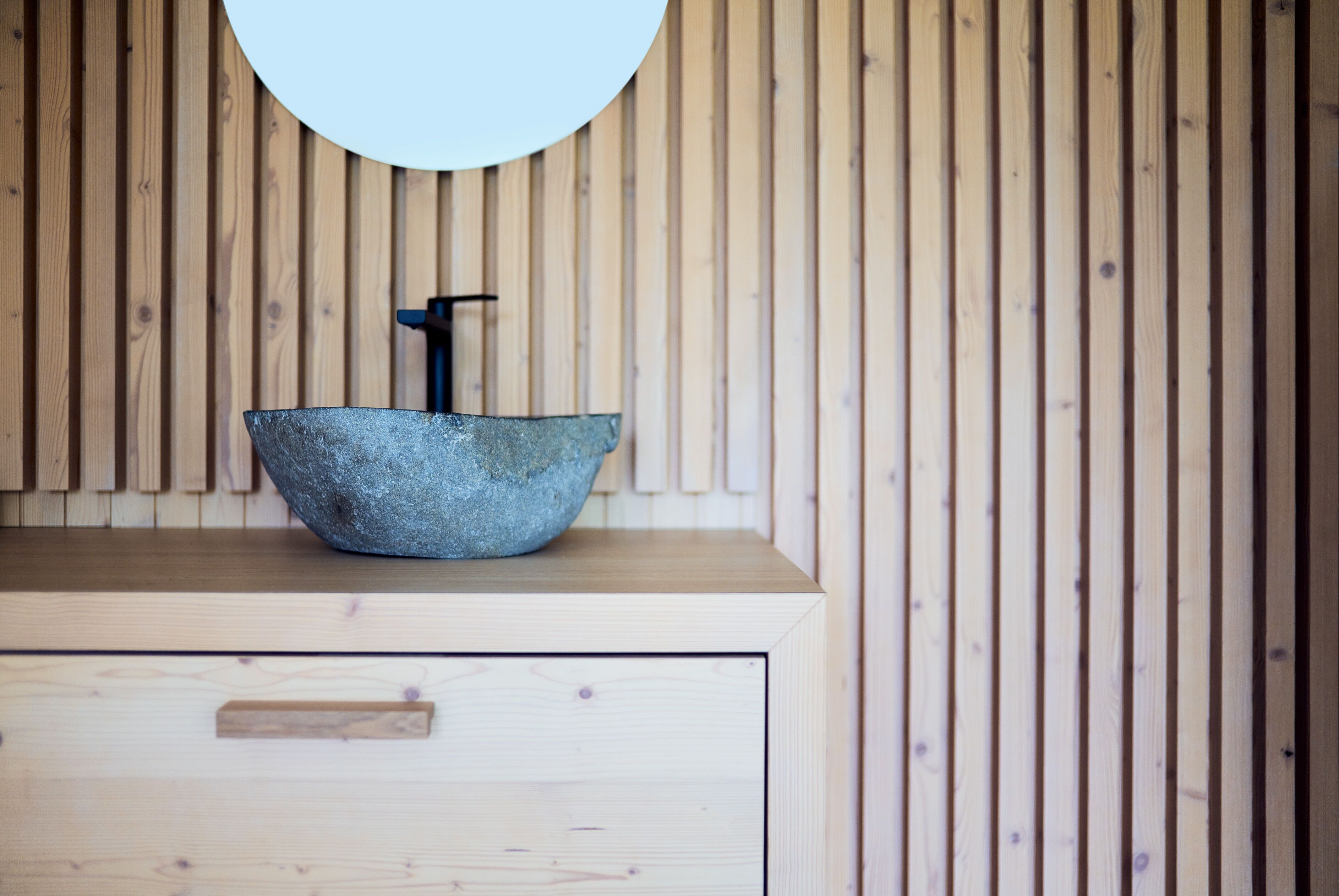 A bathroom with a wooden vanity, a stone sink, and a round mirror.