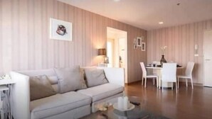 A modern living room with a sofa, a glass coffee table, and a dining area with chairs and a table. - My Resort BKK (Bangkok)