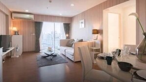A modern hotel room with a sofa, a dining table, and a TV. - My Resort BKK (Bangkok)