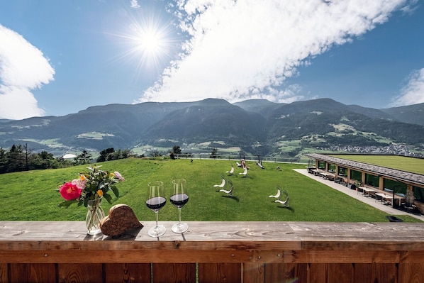 Eine malerische Außenanlage mit Bergblick, einer Holzterrasse und einem Glastisch mit Weingläsern und Blumen.