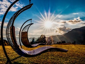 A hammock in a grassy field with mountains in the background and the sun shining.