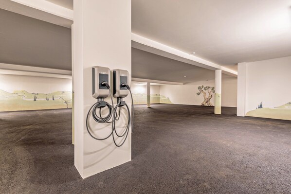 An indoor parking area with two electric vehicle charging stations, a concrete floor, and a mural on the wall.