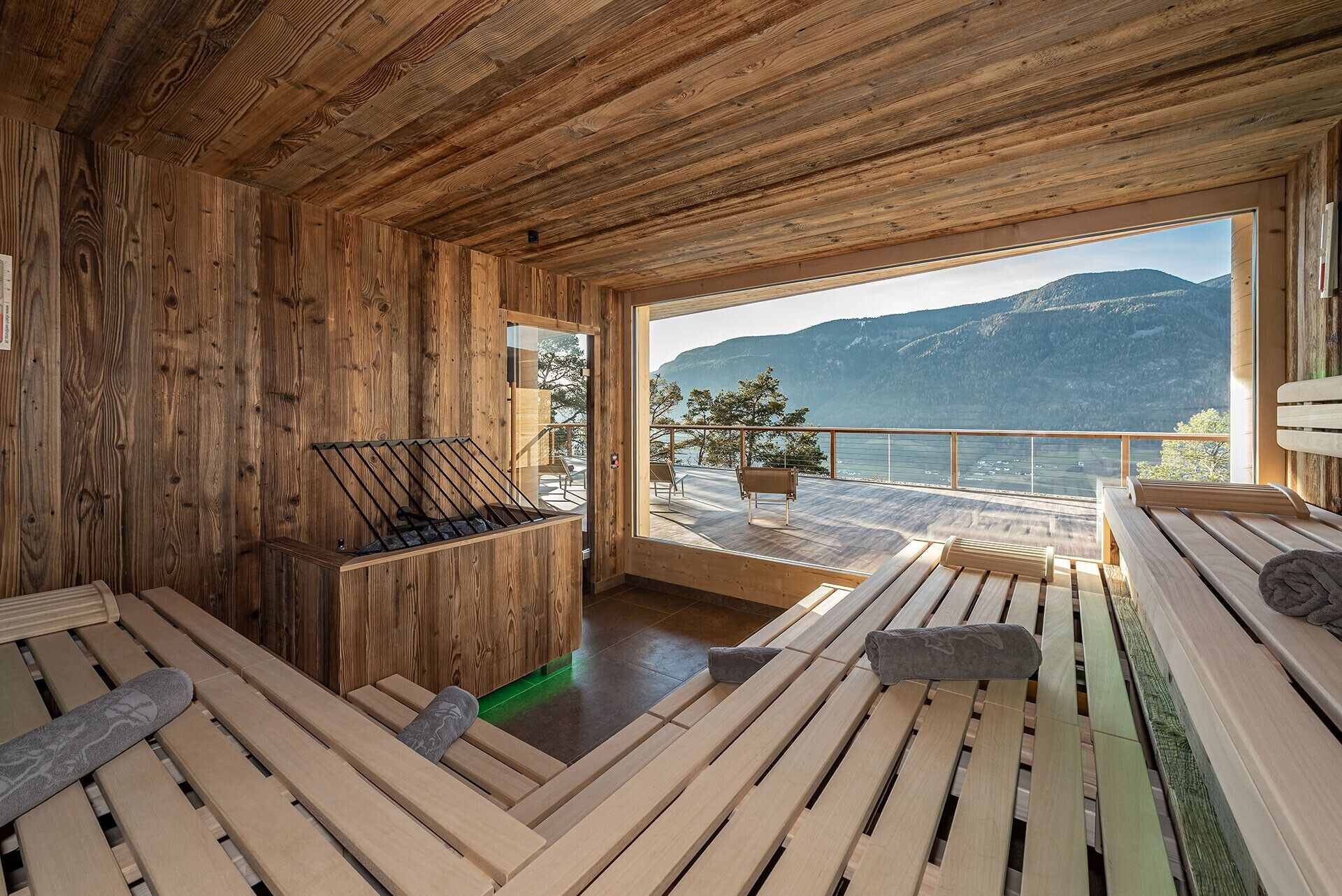 A wooden cabin with a sauna, wooden deck, and a view of mountains and water.