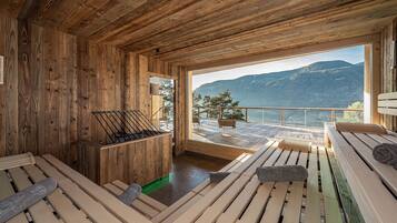 A wooden cabin with a sauna, wooden deck, and a view of mountains and water.