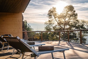 Eine Dachterrasse mit Liegestühlen, einem Tisch und Blick auf Bäume und ein Gewässer.