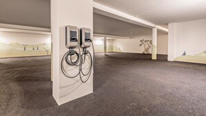 An indoor parking area with two electric vehicle charging stations, a concrete floor, and a mural on the wall.
