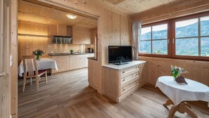 Een houten blokhut van binnen met een keuken, eethoek en een raam met uitzicht op de bergen.