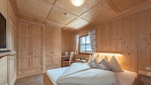 Een houten slaapkamer met een bed, een bureau en een raam met gordijnen.