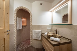 Ein Badezimmer mit Holztür, Fliesenboden, Waschbecken mit Steinplatte und Spiegel über dem Waschbecken.