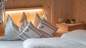 A wooden cabin interior with a bed, pillows, a nightstand, and a small potted plant.