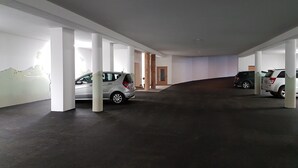 A parking garage with white pillars, a grey car, and a wooden door.