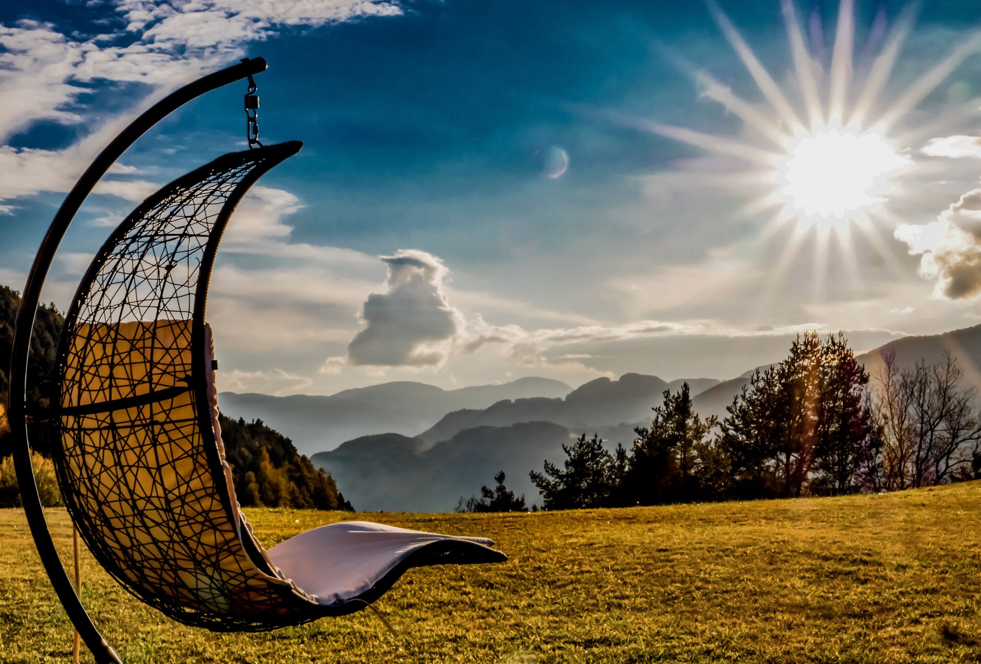 A chair with a geometric design in a grassy field with mountains in the background.
