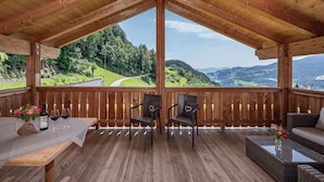 A wooden deck with a table, chairs, and a sofa overlooking a scenic landscape.