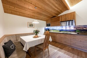 A cozy kitchen with wooden cabinets, a dining table with a vase of flowers, and a scenic mural on the wall.