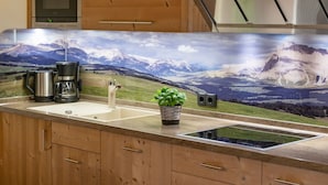 A kitchen with a mountain landscape backsplash, a coffee maker, a sink, and a small potted plant.